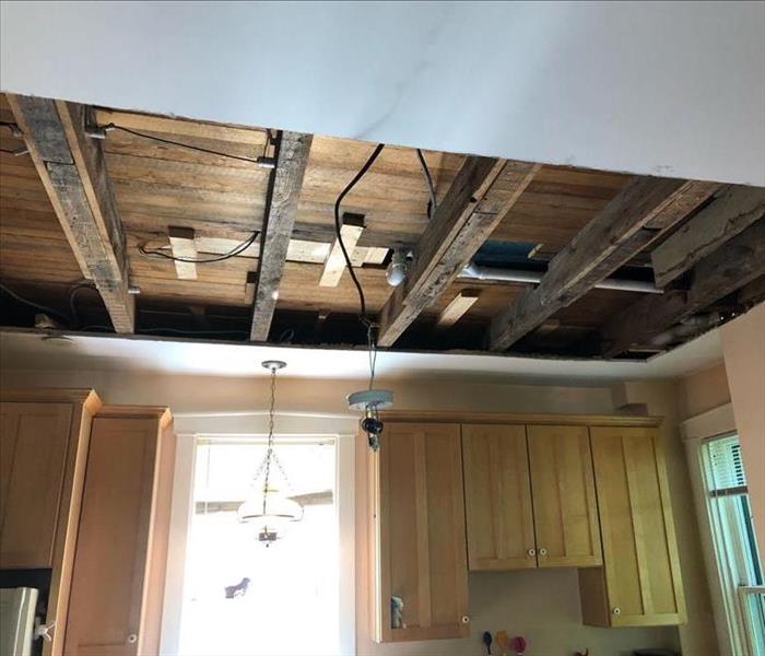 Drywall removed from the half of the ceiling in the kitchen revealing the woof joists and sub-floor above